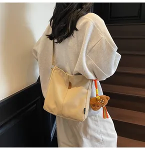 Vista dettagliata della borsa a secchiello beige in tela con ciondolo a forma di orso