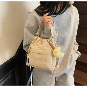 Detail of off-white nylon drawstring shoulder bag with embroidered text and moon plush charm