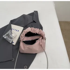 Détail du sac à main plissé rose avec chaîne argentée posé sur un blazer gris chic