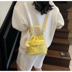 Detail of yellow nylon drawstring bucket bag with crescent plush charm on white outfit