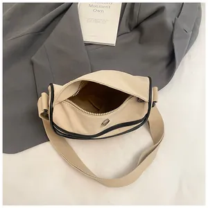 Close-up of beige canvas crescent bag with black piping detail and grey blazer styling
