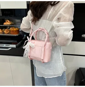 Détail d'un sac à main rose avec poignée tressée et pendentif nœud en dentelle blanche