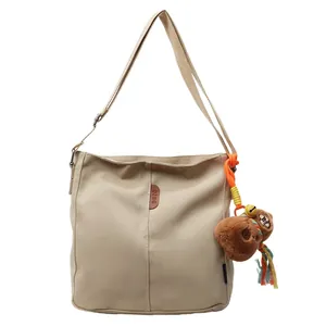 Borsa a secchiello in tela kaki con toppa in pelle e ciondolo a orsetto su sfondo bianco