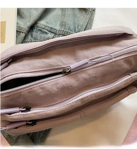 Detail of smooth purple nylon shoulder bag showing multiple zipper pockets and fabric texture