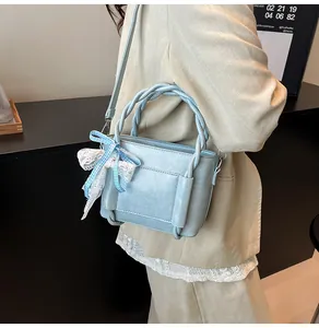 Détail d'un sac seau bleu clair avec poignée tressée et décoration de nœud à carreaux