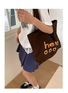 Detail of a brown canvas tote bag featuring yellow handwritten hello ooo artistic lettering