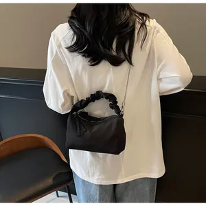 Détail d'un sac à main noir plissé avec bandoulière chaîne argentée sur chemise