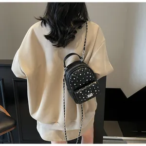 Detail of black quilted mini backpack with pearl accents and metal chain strap on model