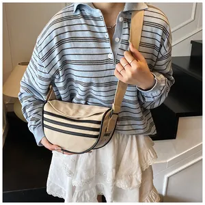 Detailed shot of beige canvas crescent bag with black stripes on striped knit shirt