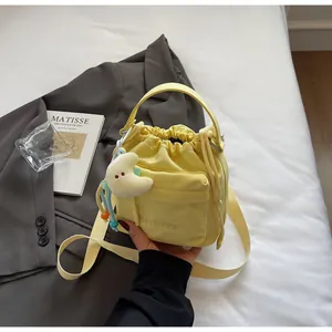 Detail of light yellow nylon drawstring bucket bag with plush moon charm and crossbody strap