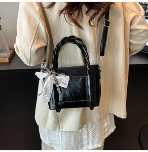 Mannequin portant un sac bandoulière noir brillant avec poignée tressée et dentelle
