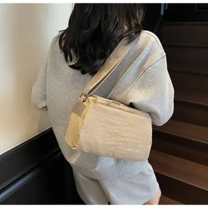 Rear view of a model wearing a lightweight beige nylon crossbody bag with embroidery