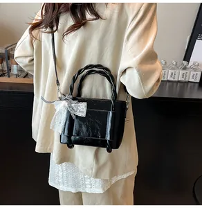 Détail du sac à main noir brillant avec poignées tressées et nœud en dentelle