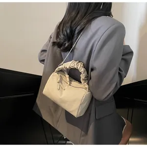 Détail du sac polochon beige avec poignée plissée et chaîne en métal porté par un modèle