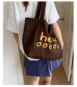 Detail of dark brown canvas tote bag featuring yellow hellooooo slogan on model's shoulder