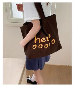 Brown canvas tote bag with yellow hello print shown on model with casual white t-shirt