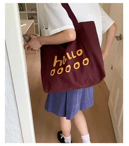 Detail of burgundy canvas tote bag with yellow hello text print worn over the shoulder