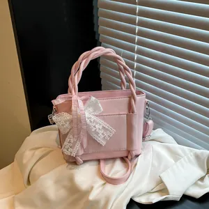 Sac seau en similicuir rose avec poignée tressée et nœud en dentelle sur tissu blanc