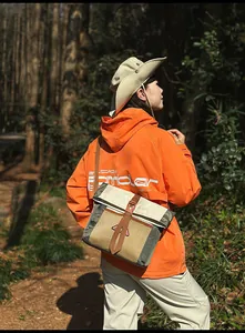 Outdoor-Enthusiast trägt orangefarbene Windjacke und Kontrast-Umhängetasche im Freien