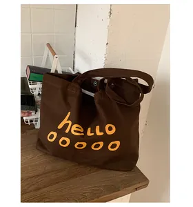 Detail of dark brown canvas tote bag with yellow hello print and metal snap closure