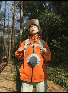 Outdoor-Look mit leuchtend oranger Windjacke und grauem Rucksack auf einem Waldweg
