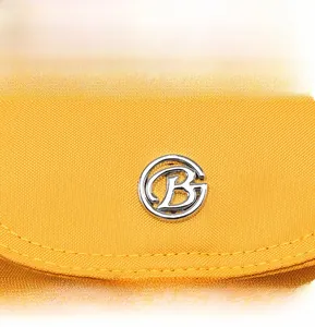 Detailed macro view of yellow canvas bag featuring a circular silver metal B logo charm