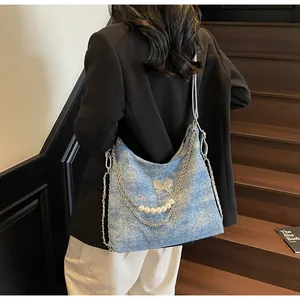 Detail of light blue denim tote with silver chains, butterfly and pearl ornaments