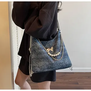 Detail of blue denim shoulder bag with sparkling finish, gold butterfly and pearl chain