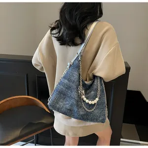 Detail of blue denim tote bag with silver chain straps and elegant pearl decorations