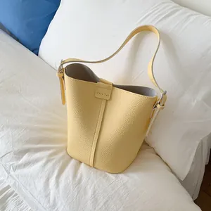 Sac seau jaune clair avec motif litchi et étiquette en cuir sur fond blanc épuré