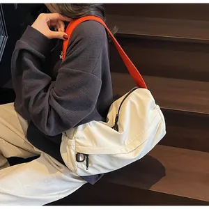 Detail of minimalist cream crossbody bag with vibrant orange strap and black zipper pocket