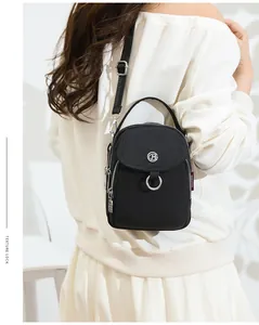 Detail of a black nylon crossbody bag with silver zippers and side fabric tag detail
