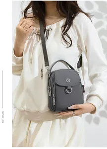 Detail view of dark grey nylon crossbody bag with metallic logo and multi-zipper layers