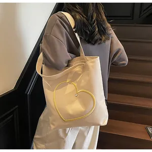 Detail of a cream canvas tote bag with yellow heart embroidery worn by a model
