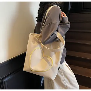 Detail of beige canvas tote bag with yellow heart embroidery and silver metallic heart charm
