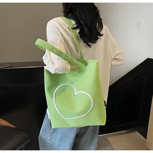 Detail of lime green canvas tote bag featuring embroidered white heart and shoulder straps