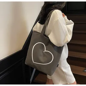 Detail of grey canvas tote bag with heart embroidery shown on shoulder by model