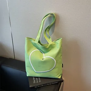 Light green canvas tote bag with heart embroidery leaning against a textured wall