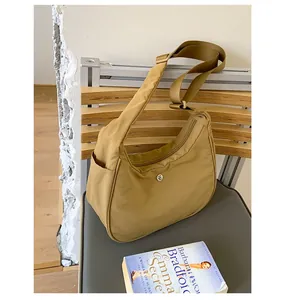Détail d'un sac demi-lune en nylon kaki avec logo et bandoulière sur une chaise grise