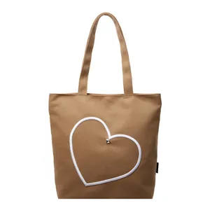 Brown canvas tote bag with white heart embroidery and a central silver metal stud