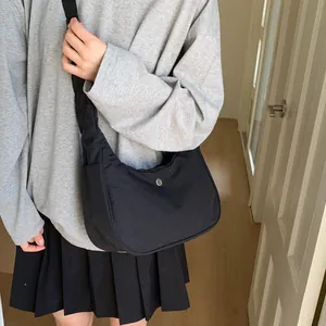 Gros plan sur un sac bandoulière noir en forme de croissant porté avec un style décontracté