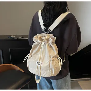 Back view of a beige drawstring backpack on a model showing wide straps and metal clips