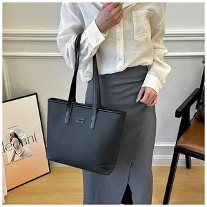 Detail of black lychee grain leather tote bag with reinforced handles and brand plaque