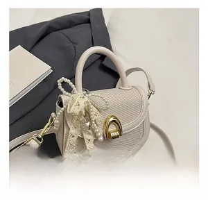 Détail du sac selle beige avec texture tressée et boucle fer à cheval dorée et perles