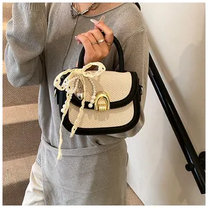 Détail du sac selle tissé avec fermoir en U doré, breloques perles et nœud en dentelle