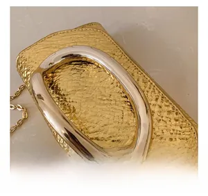 Macro detail of gold snake-embossed leather square bag with large U-shaped silver handle