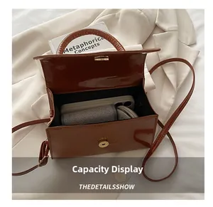 Détail montrant la capacité intérieure du sac en cuir verni marron sur un blazer
