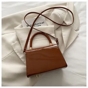 Détail d'un sac bandoulière en cuir verni marron foncé avec ferrures en métal doré