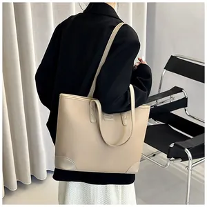 Detail view of large beige pebble leather tote bag with thin straps and metal brand logo