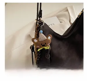 Close-up of brown plush bear charm with birthday hat hanging on leather handbag